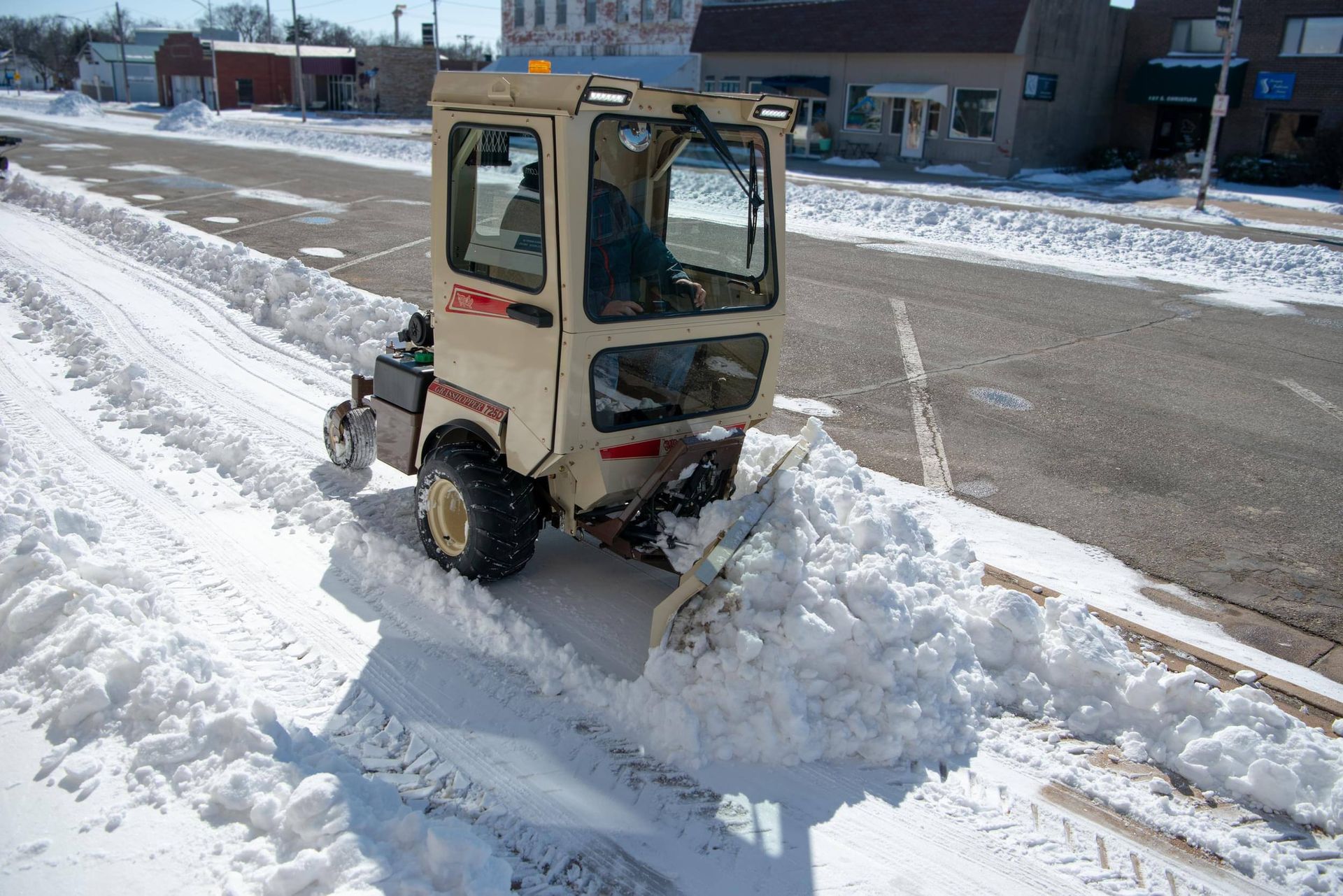 Grasshopper 725D with an enclosed cab pushing snow with a V-plow along a small-town street.