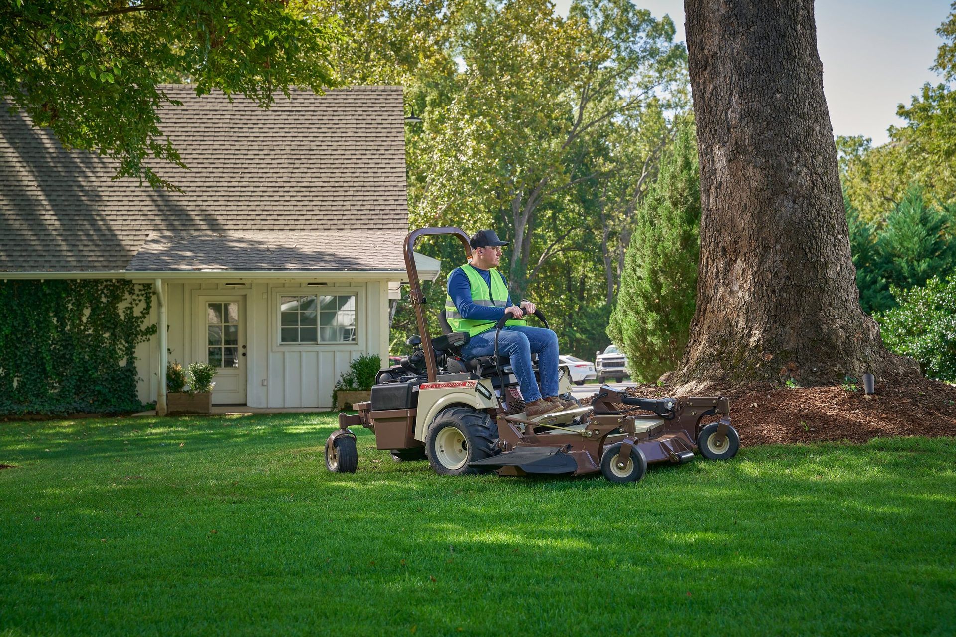 Grasshopper 735 FrontMount mower cutting a green lawn beside a cottage and a large tree.