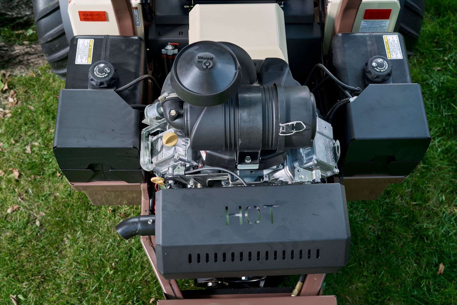 Overhead view of a mower's Kawasaki engine, twin fuel tanks, and muffler shield.