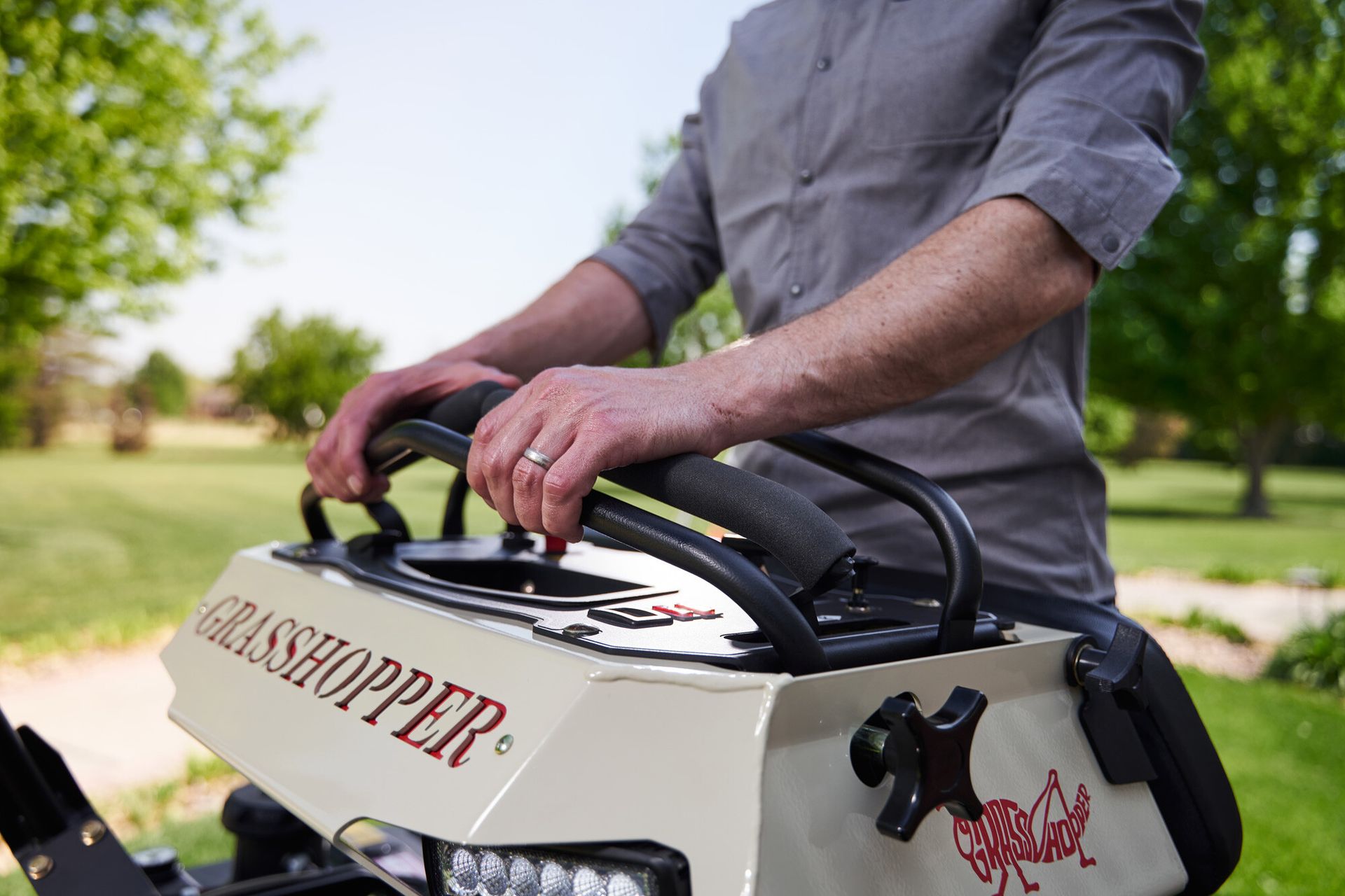 Operator's hands gripping the padded control bar of a Grasshopper stand-on mower.
