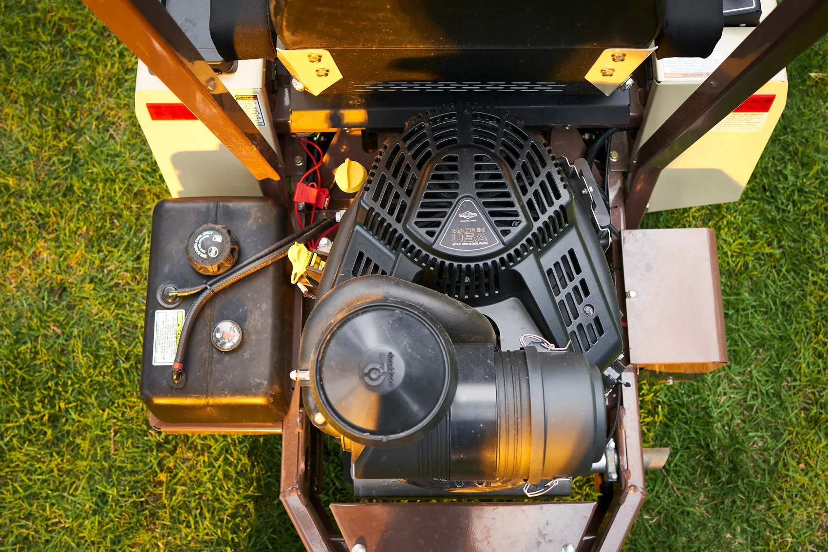 Top-down view of a mower's engine bay showing the air cleaner, fuel tank, and decals.