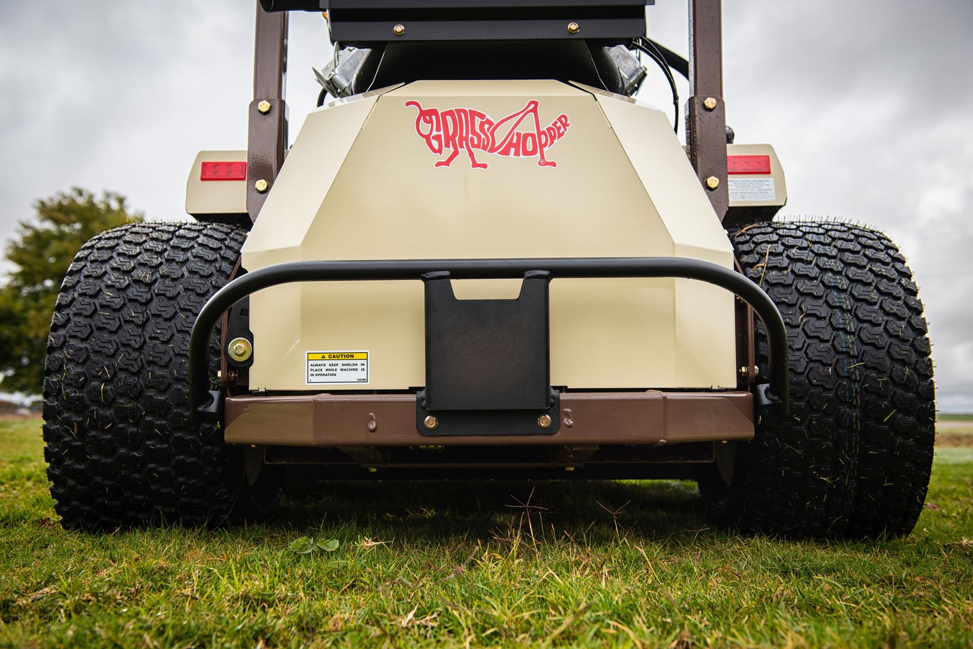 Rear view of a Grasshopper mower's tan engine cover, caution decal, and knobby turf tires.