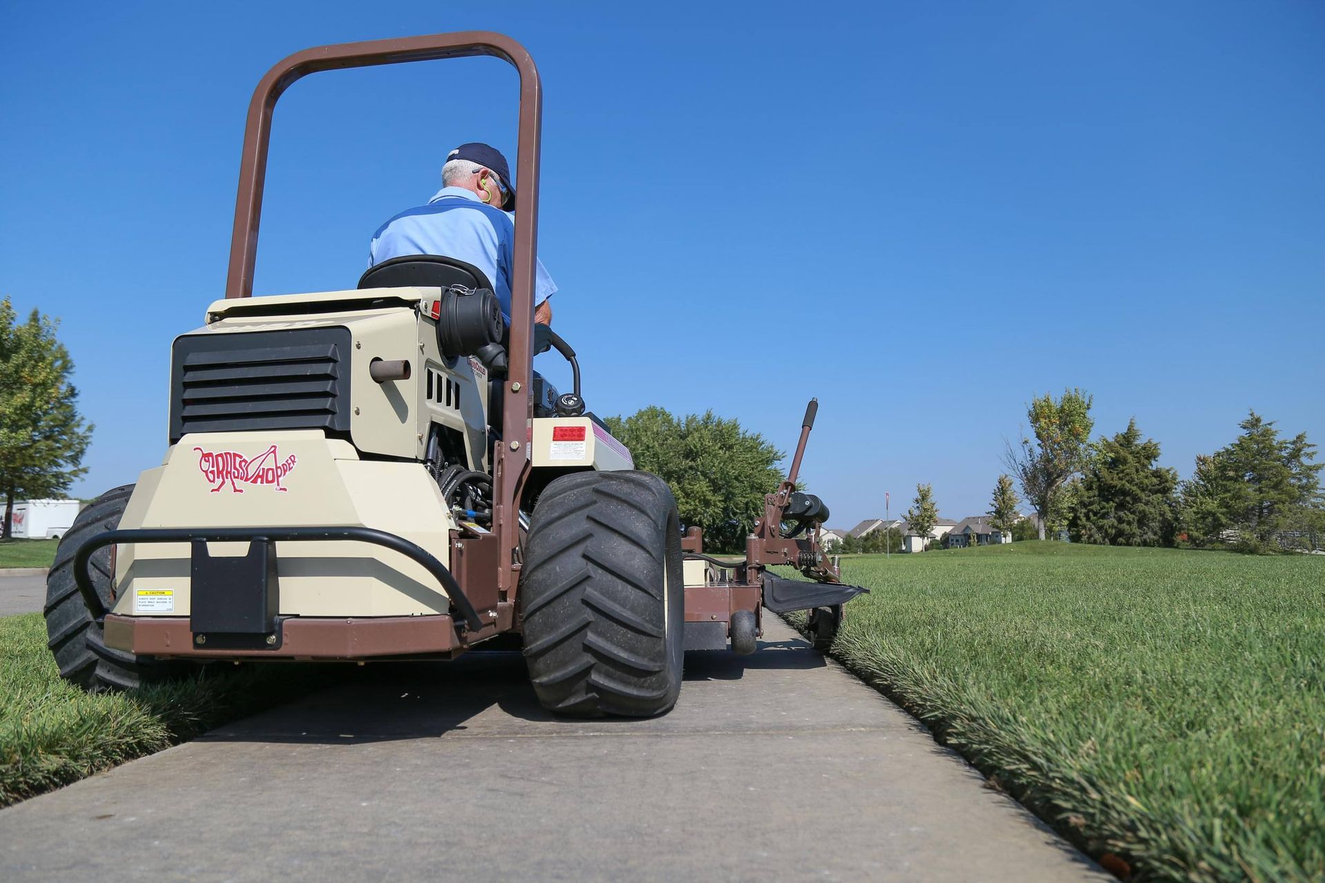 Low-angle rear view of an operator edging a sidewalk with a Grasshopper mower attachment.