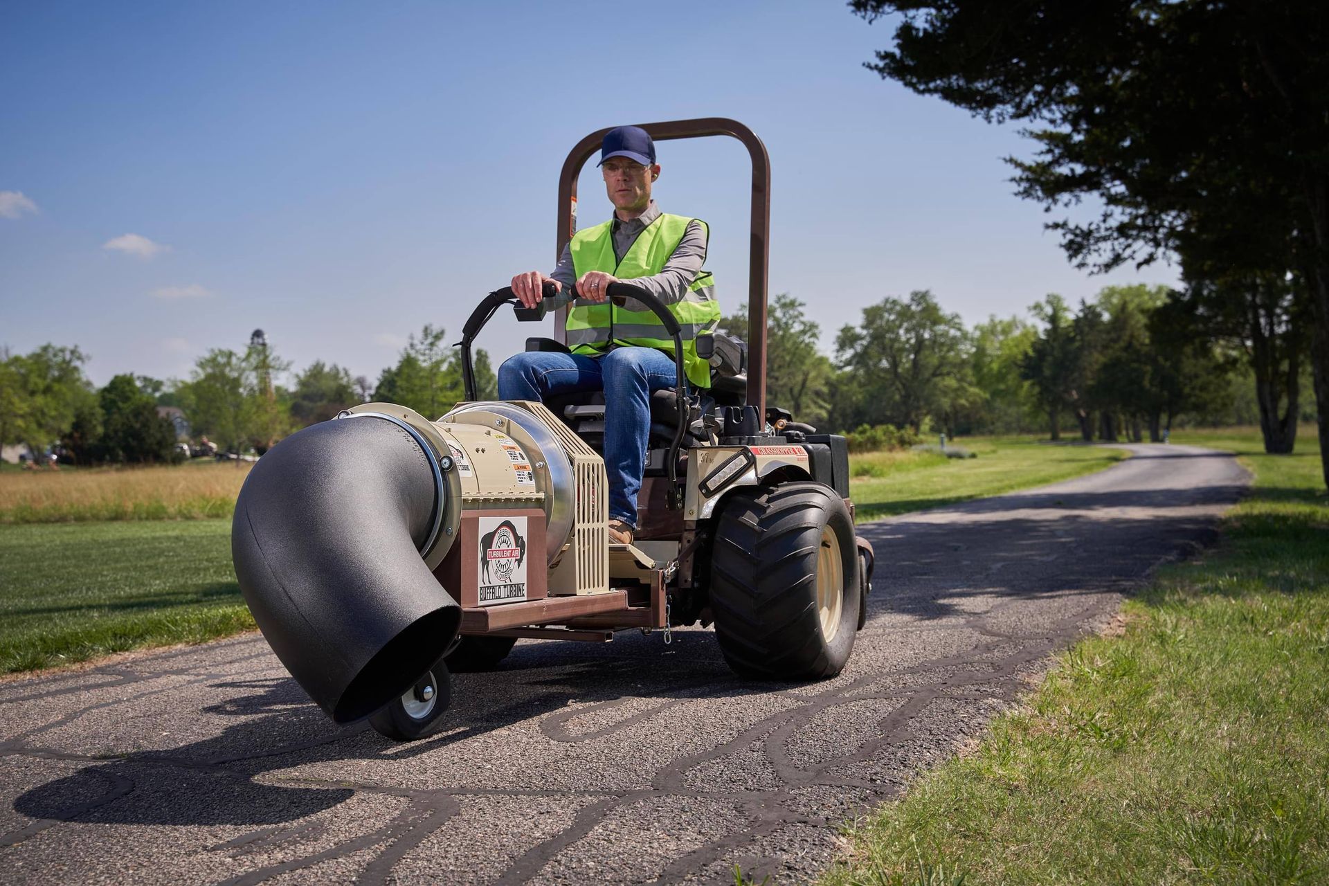 Operator in a hi-vis vest driving a Grasshopper mower fitted with a large turbine blower attachment.