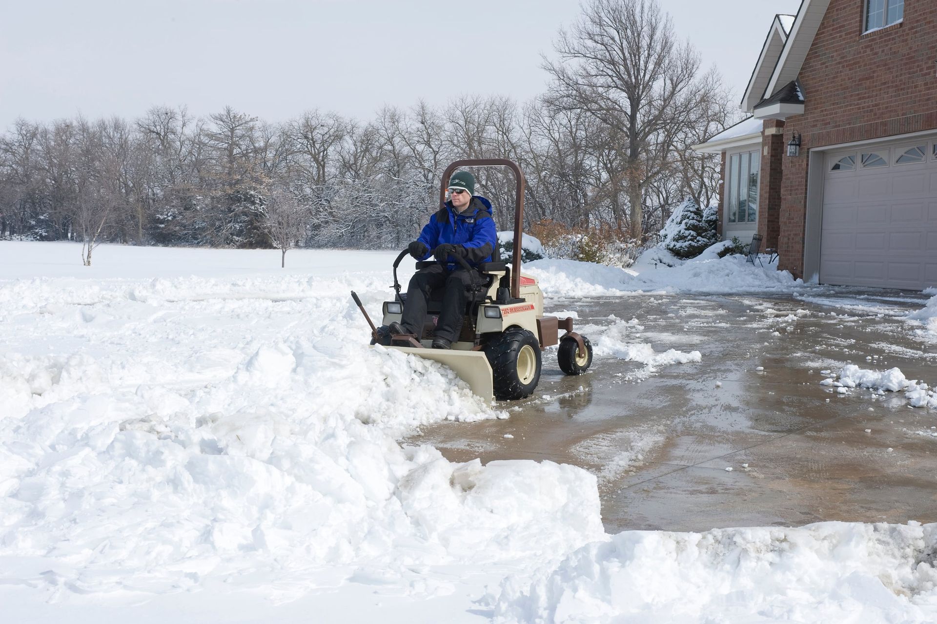 Operator plowing snow from a driveway with a Grasshopper 725D and front blade.