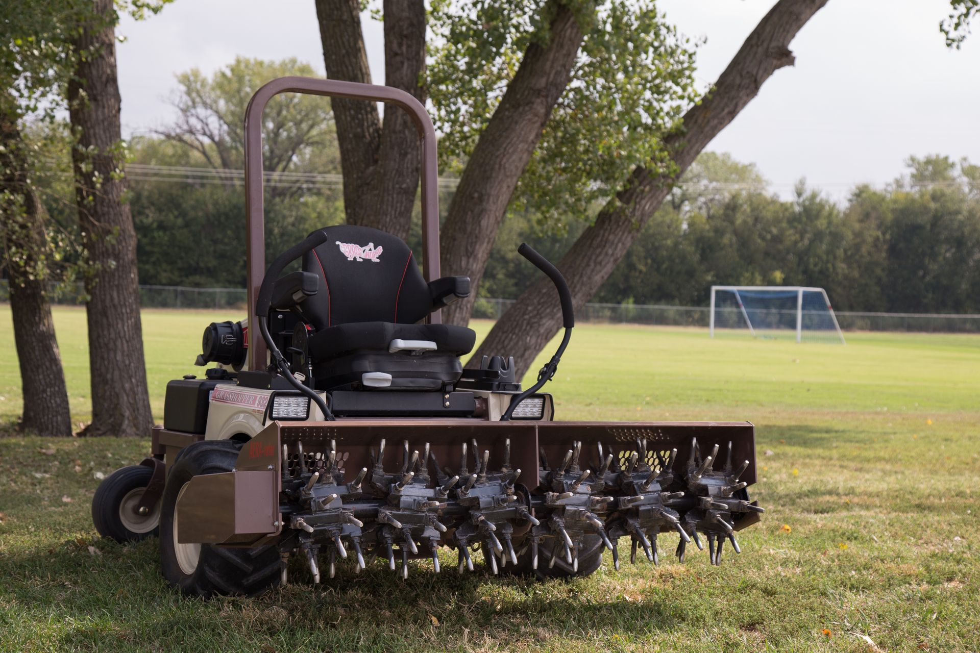 Grasshopper mower fitted with an AERA-vator attachment, its spiked rollers resting on turf.