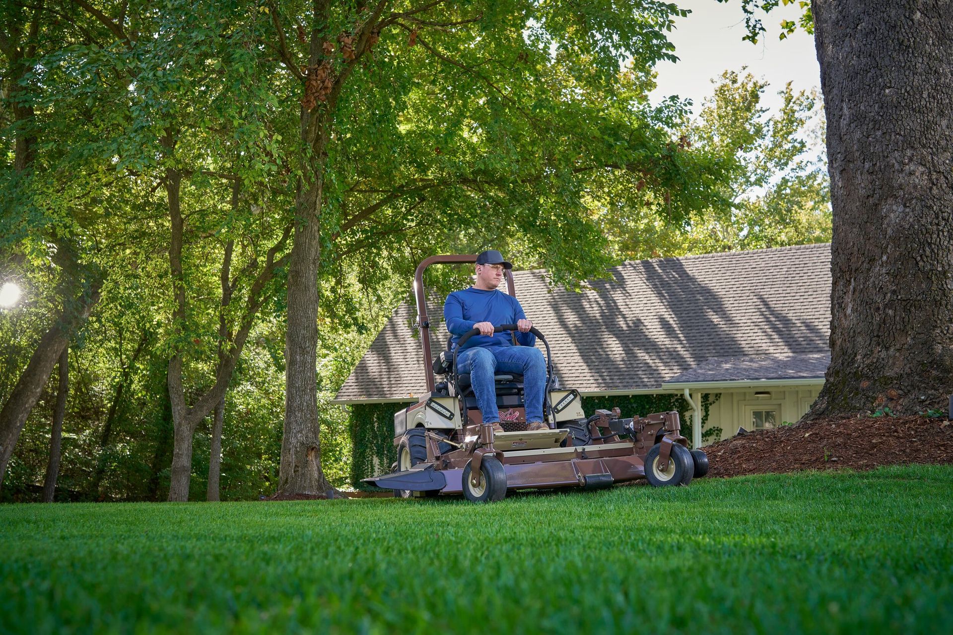 Man mowing a lawn on a Grasshopper FrontMount mower beside a freshly mulched tree bed.