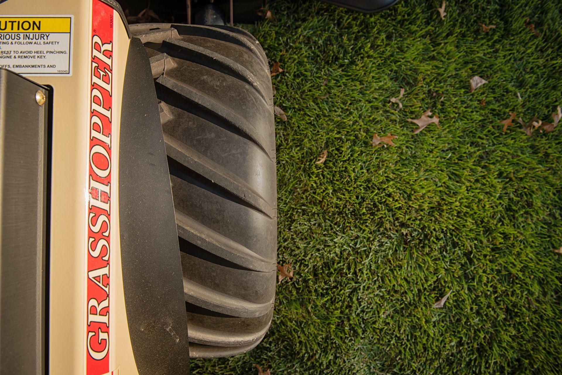 Close-up of a Grasshopper mower's ribbed rear drive tire and fender on turf.
