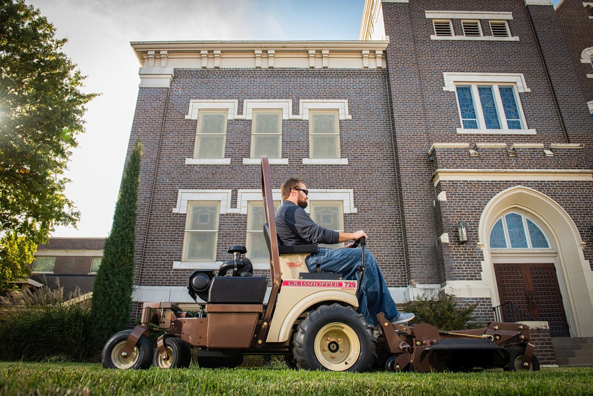 Operator on a Grasshopper 729 FrontMount mower passing a brick building with stained-glass windows.