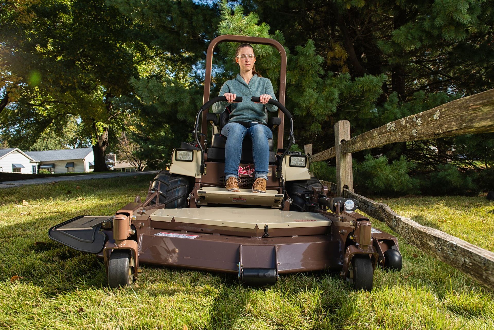 Woman in safety glasses and ear plugs behind the wide out-front deck of a Grasshopper mower.