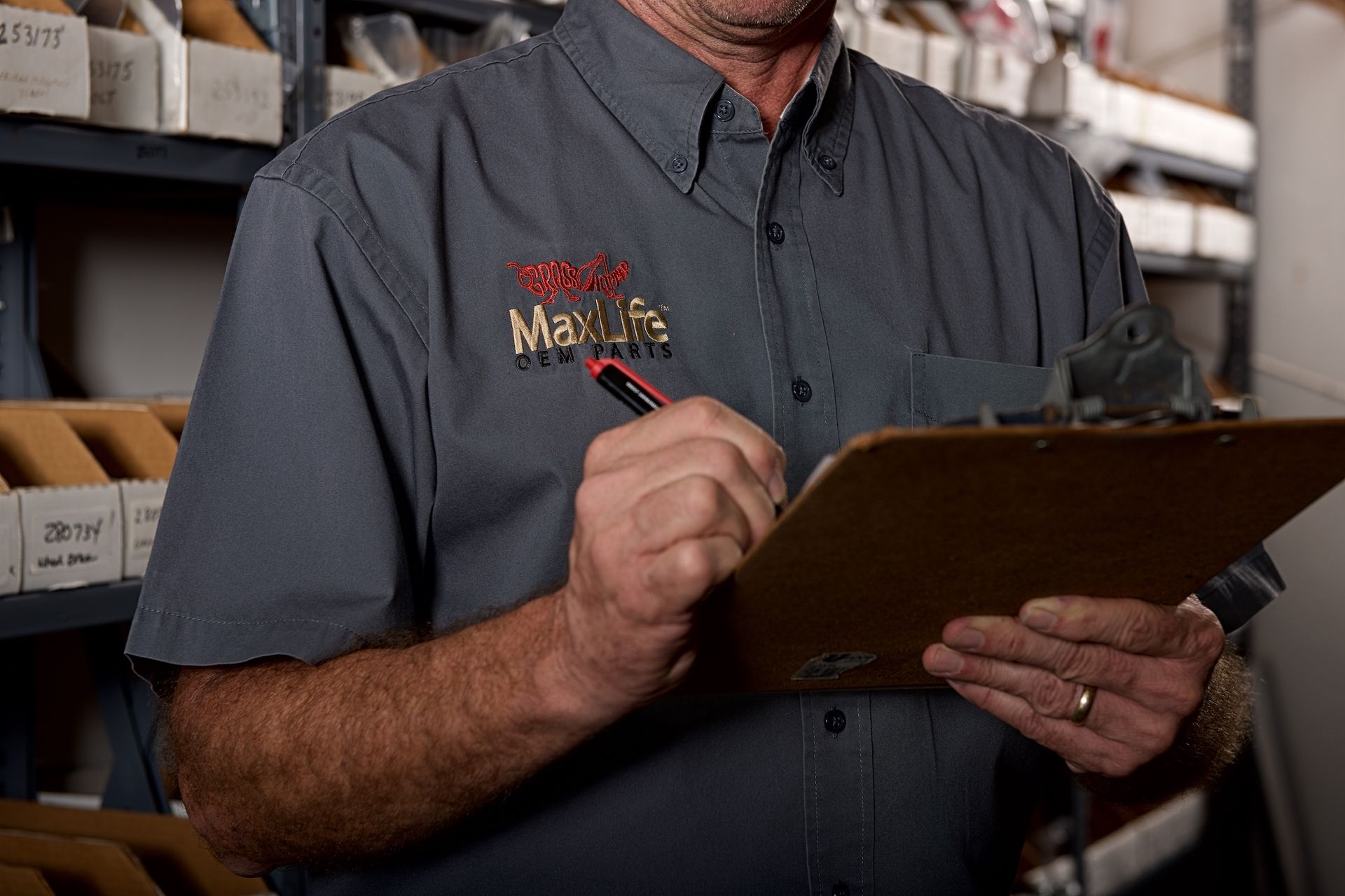 Parts staffer in a Grasshopper MaxLife OEM Parts shirt writing on a clipboard among stocked shelves.