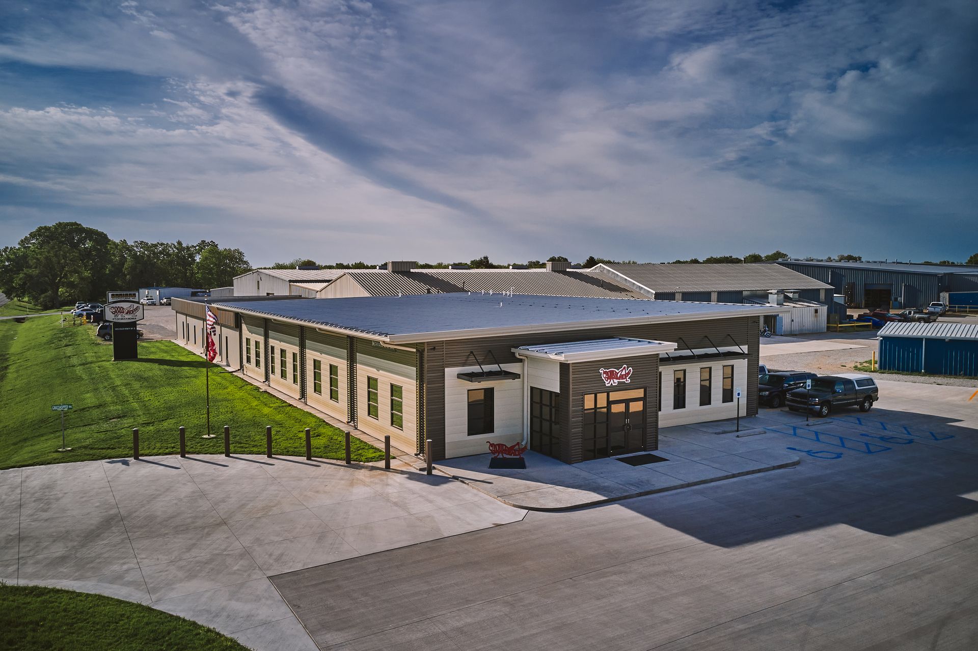 Aerial view of the logo-marked Grasshopper headquarters entrance with factory buildings and flagpole behind.
