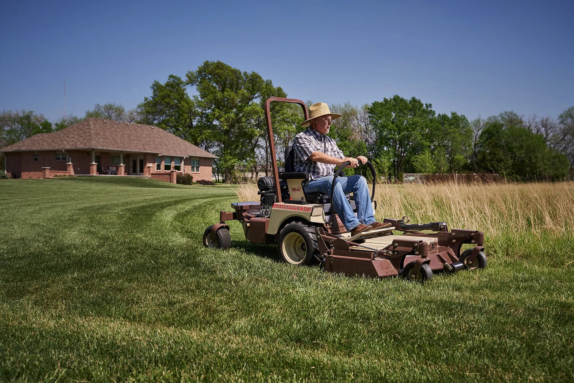 Man in a straw hat mowing striped turf on a Grasshopper 526V FrontMount mower.