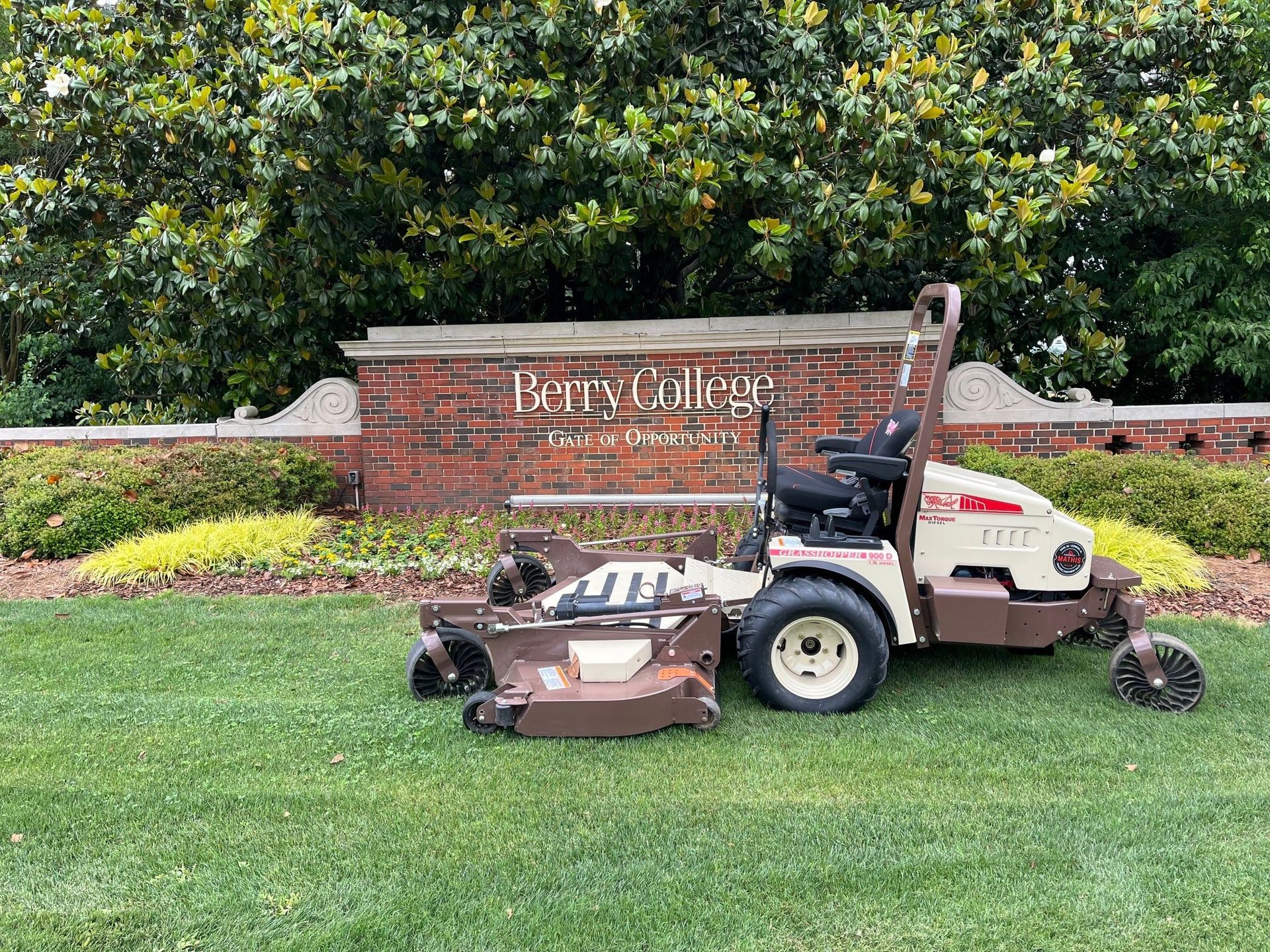Grasshopper 900D FrontMount mower parked on mown turf beside the brick Berry College entrance sign.