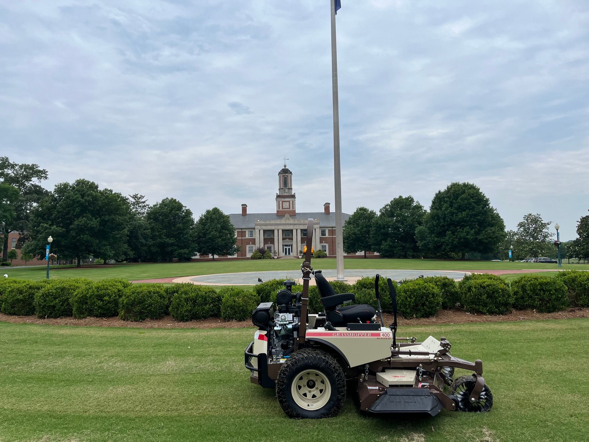 Grasshopper 400 FrontMount mower parked on a mown campus lawn before a brick building and flagpole.