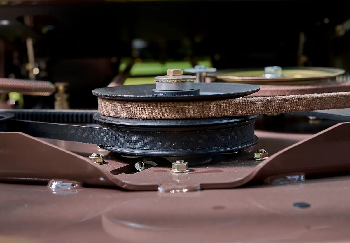 Close-up of a mower deck spindle pulley with two drive belts and mounting bolts.