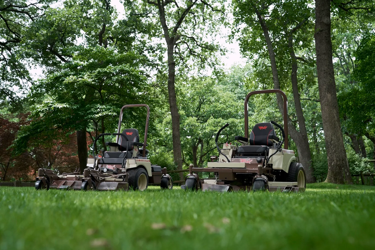 Two Grasshopper FrontMount zero-turn mowers parked side by side on a shaded lawn.