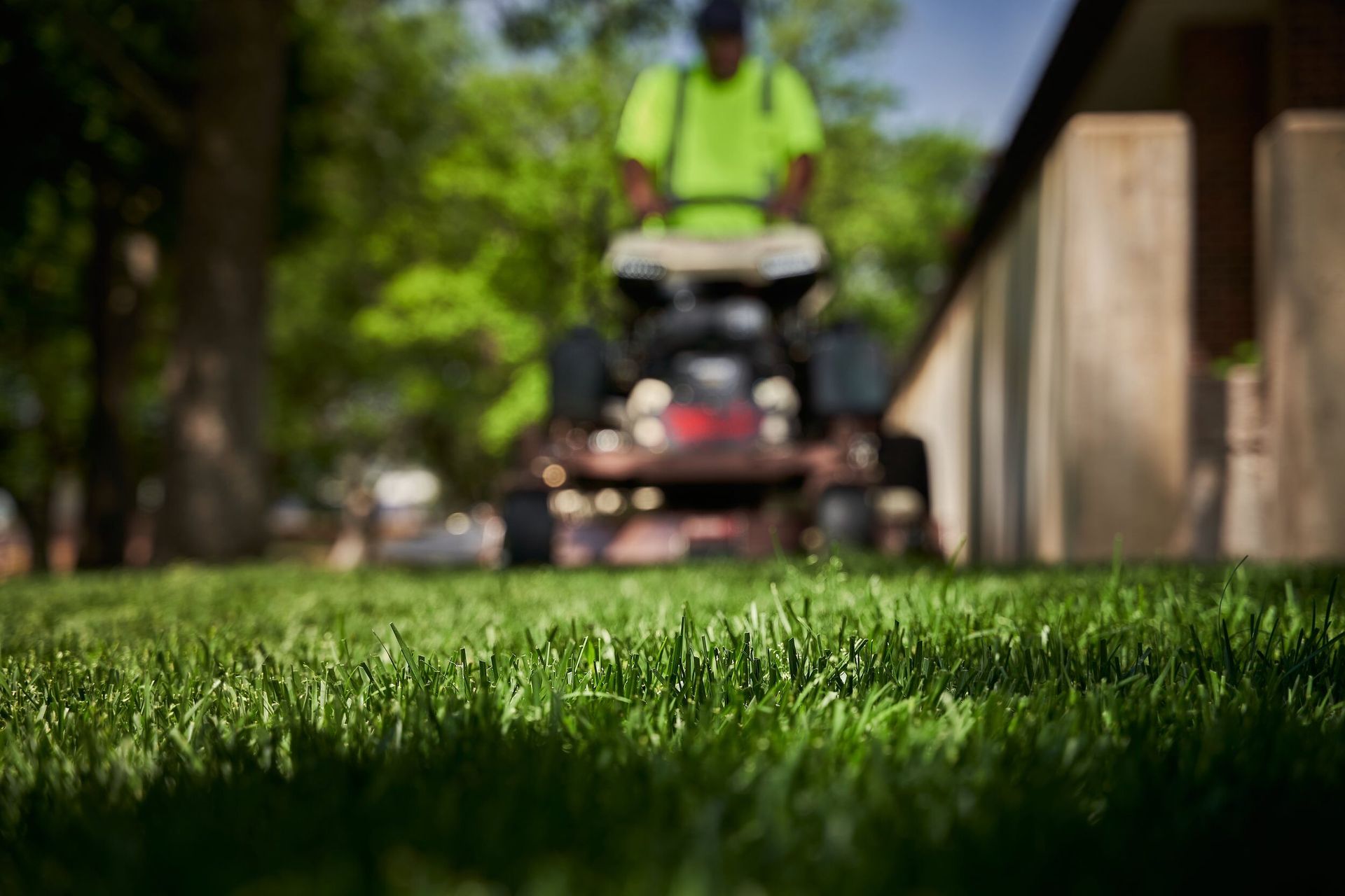 Ground-level view of cut turf with a blurred operator on a Grasshopper stand-on mower.