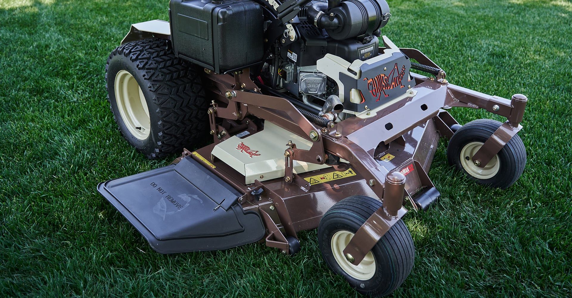 Grasshopper stand-on mower parked on green grass, seen from above with its deck and discharge chute.