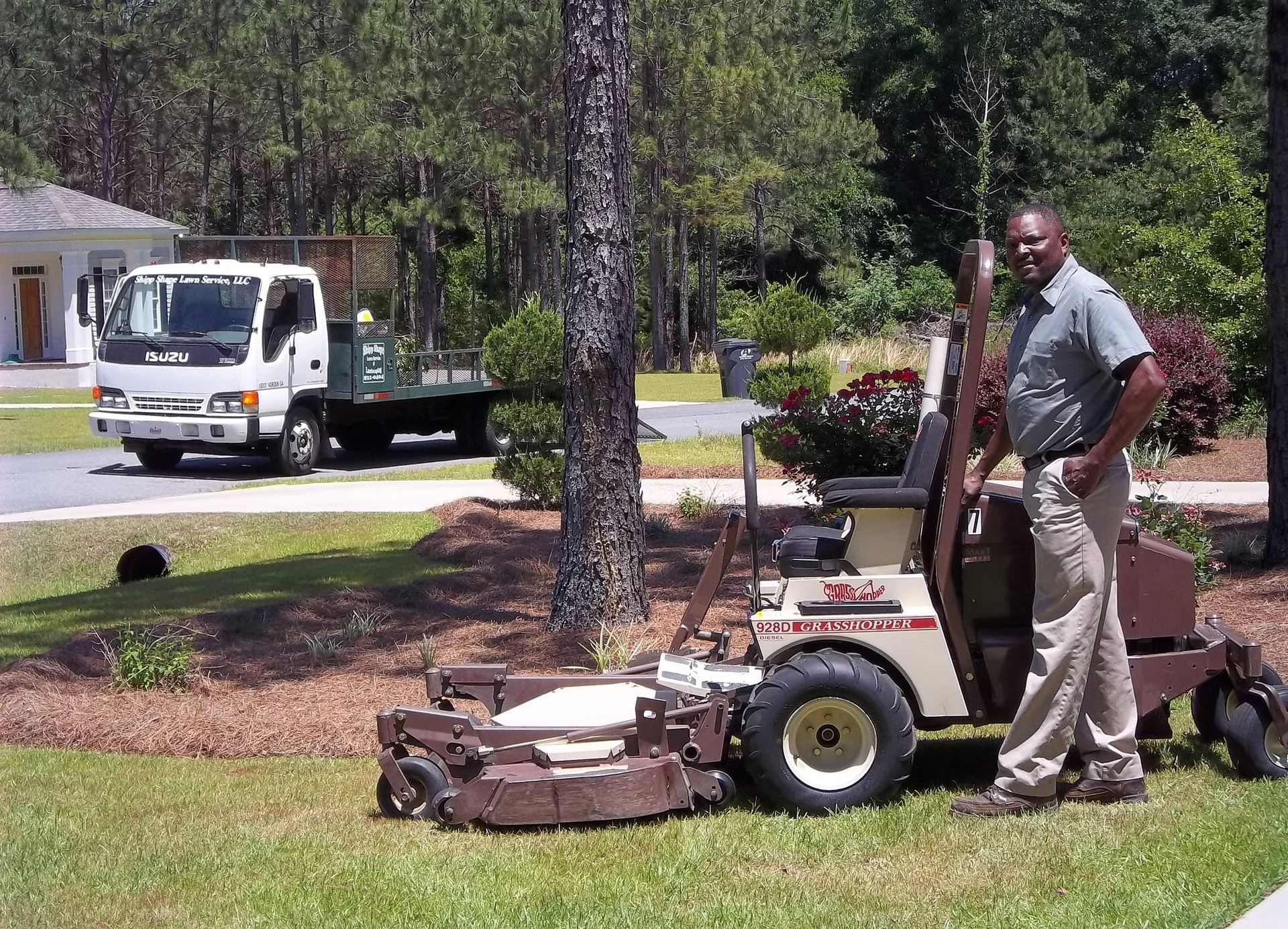 Landscaper standing beside a Grasshopper 928D diesel FrontMount mower with his lawn service truck behind.