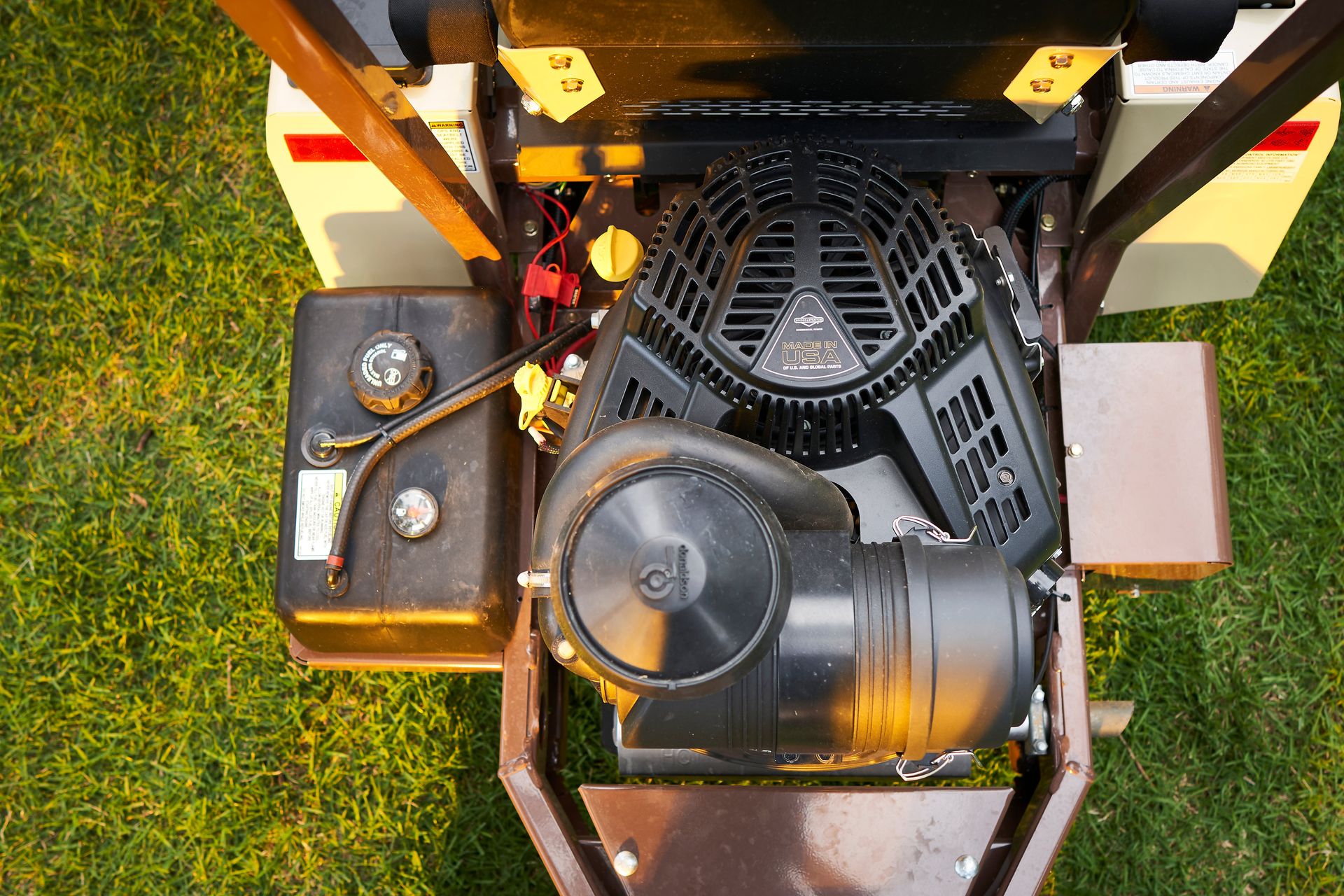 Top-down view of a mower's Briggs and Stratton engine, air filter housing, and fuel tank.