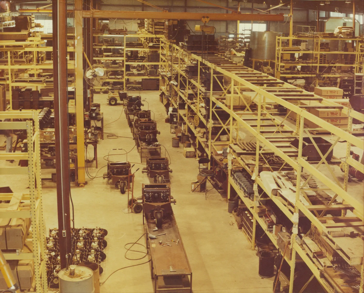 Elevated view of a vintage factory floor with yellow steel racking and partly assembled mower frames.