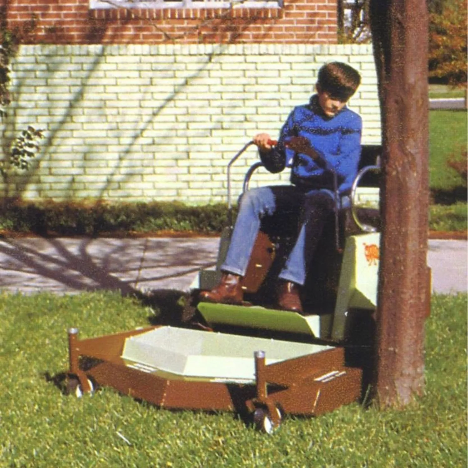 Young operator on an early out-front deck mower trimming grass close to a tree trunk.