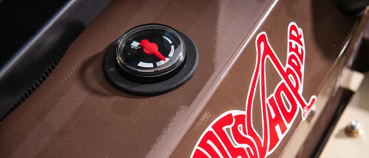 Close-up of a round fuel gauge on a brown Grasshopper mower panel beside the red logo.