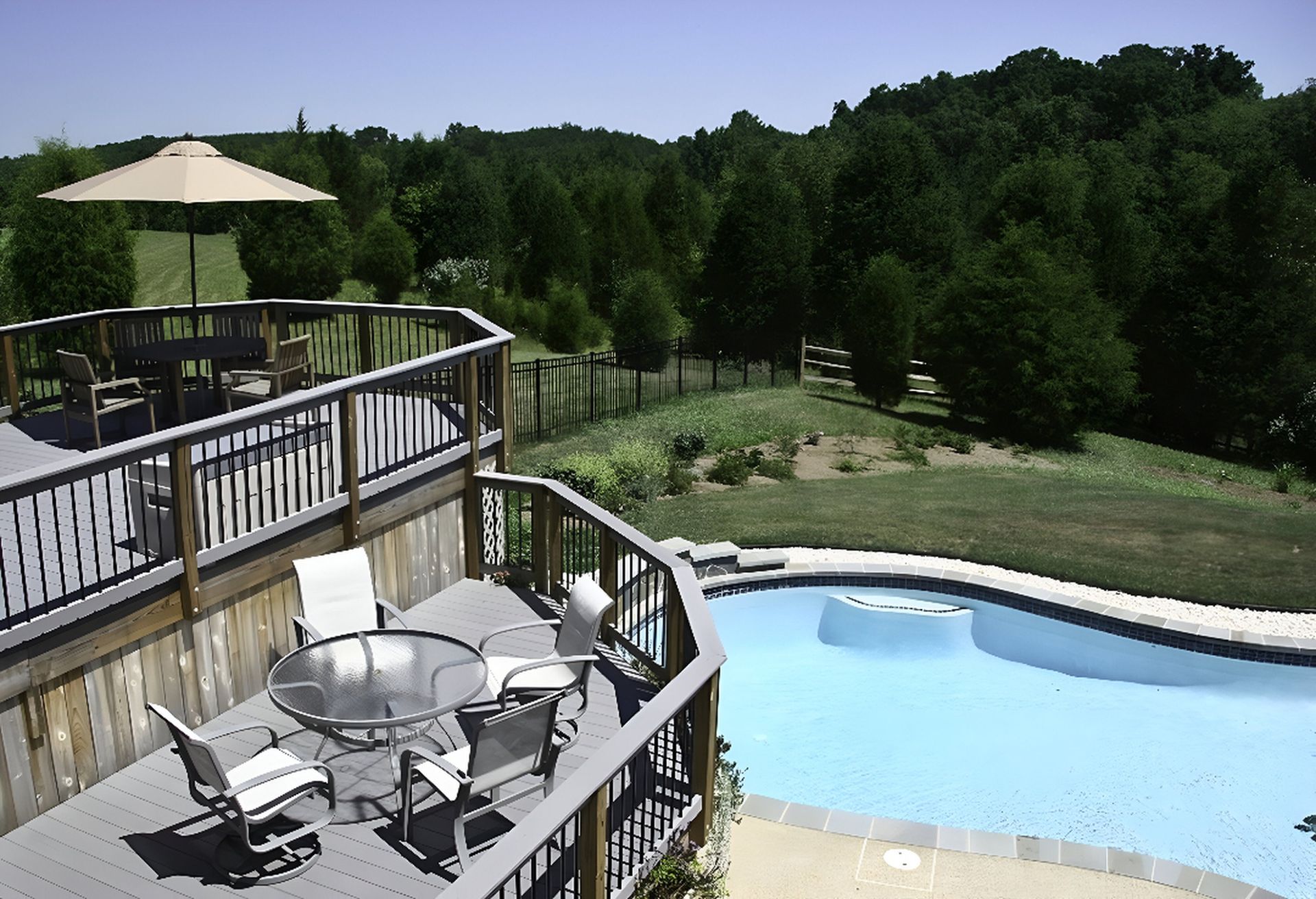 Two-tier wooden backyard deck with patio furniture overlooking a curved swimming pool and lawn.