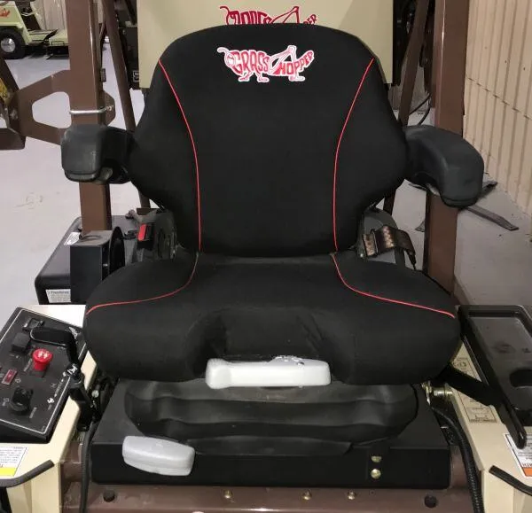 Grasshopper suspension seat with red piping and padded armrests, mounted beside the operator control panel.