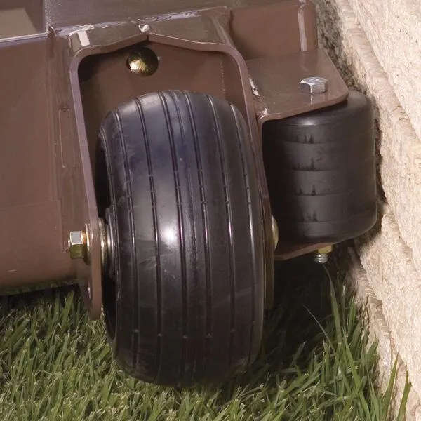 Close-up of a mower deck's caster wheel and black trim roller riding against a stone wall.
